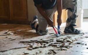 A home renovator, manually removing tile flooring from concrete slab